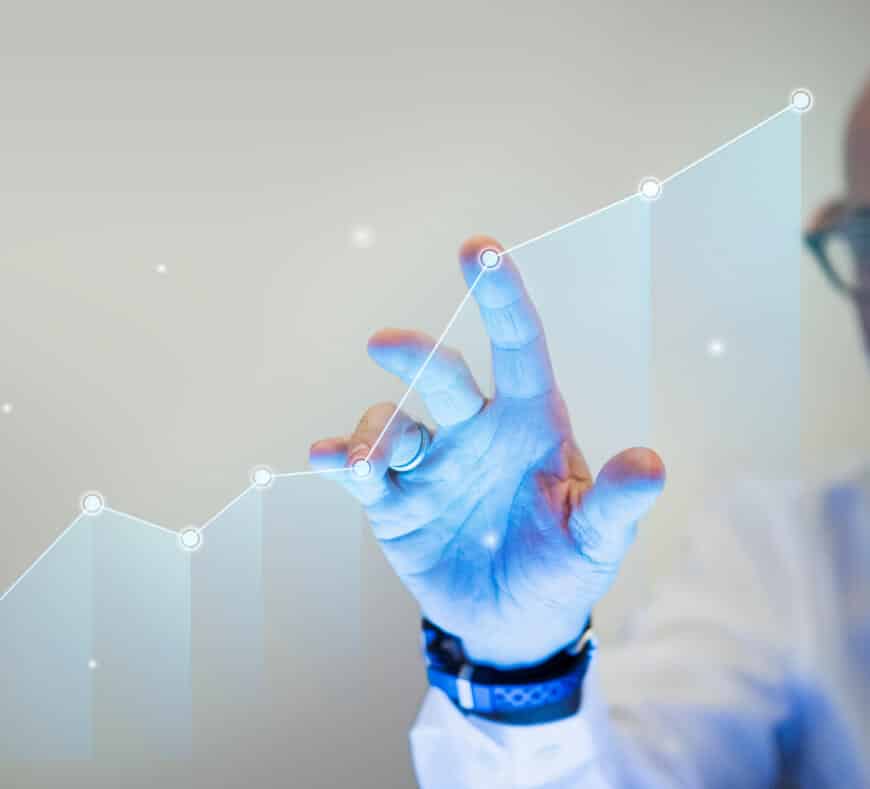 A person’s hand touches a glowing upward-trending line graph, symbolizing growth or success. The background is blurred, and only part of the person’s face and glasses are visible.